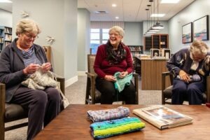 Three women sitting around a coffee table laughing while knitting