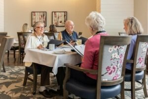 Three older women and one older gentleman chatting at a dining room table while looking at menus