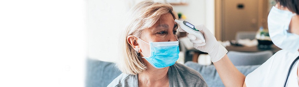 nurse taking the temperature of a woman with a medical mask on